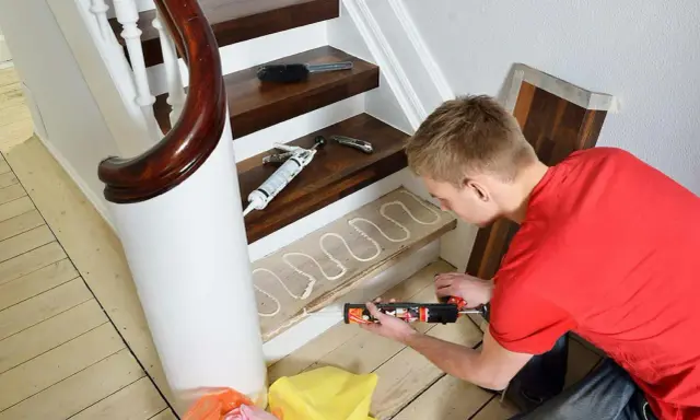 Man i röd tröja applicerar lim på trappsteg för att byta trappa. Limmet läggs i ett vågmönster.