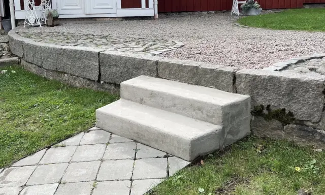 Nya gjuta trappsteg i betong leder upp från en stenlagd gång.