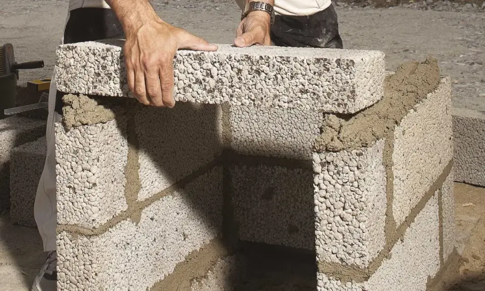 Händer lägger lecablock direkt på marken, bygger en mur med cement.