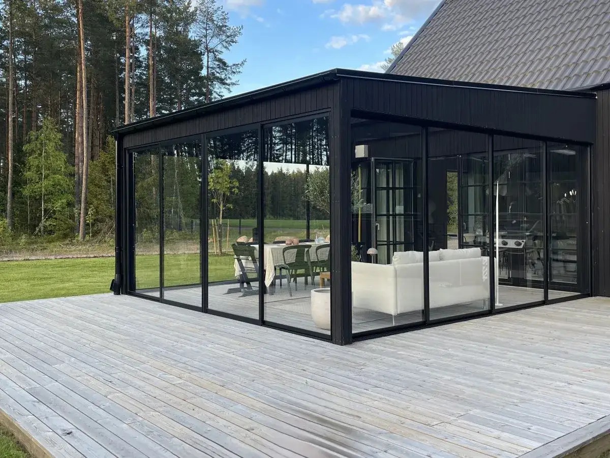 Gr&aring; tr&auml;altan med en modern glasveranda. Tr&auml;materialet p&aring; altanen ger en naturlig k&auml;nsla mot den omgivande skogen.