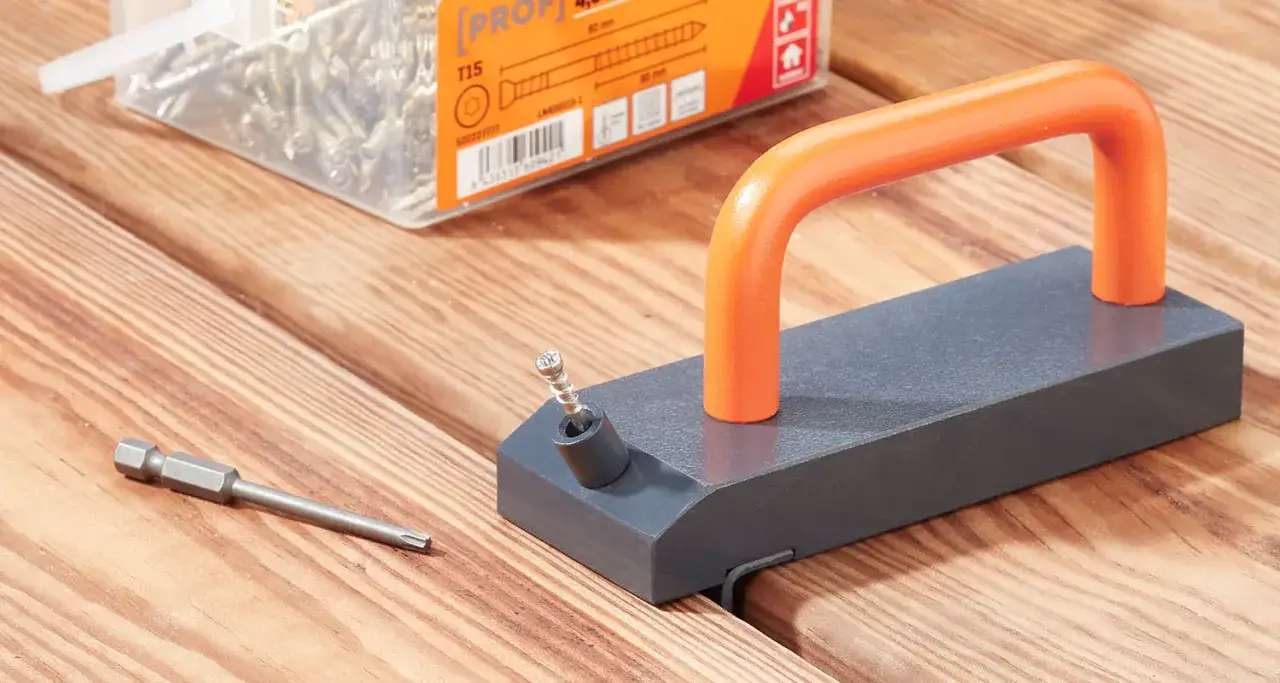 Verktyg för att skruva trall från sidan. En skruv och bits ligger bredvid en jig med orange handtag.