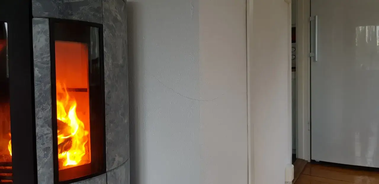 Eld i kaminen värmer rummet. En spricka syns på väggen, kanske dags att måla cellplast?