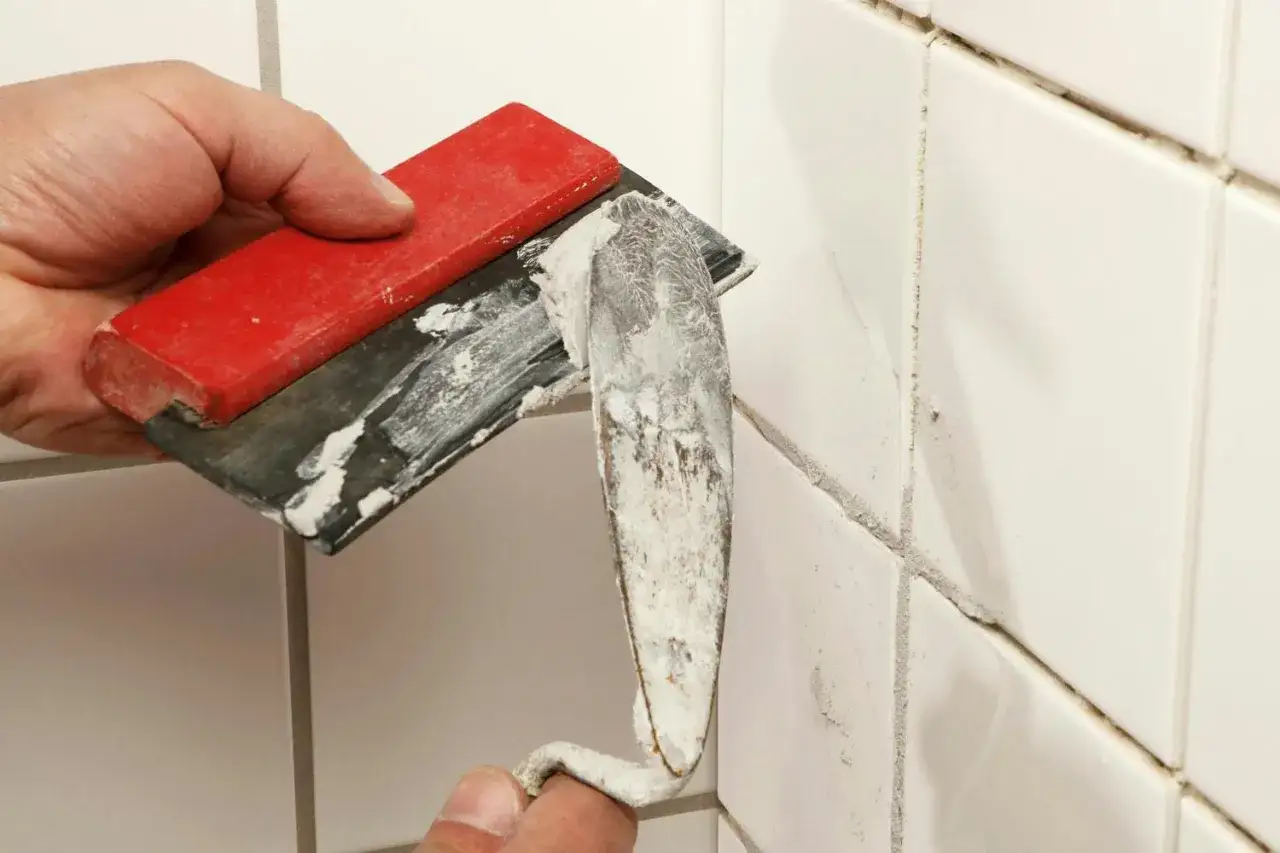 En hand använder en spackel för att foga om kakel.