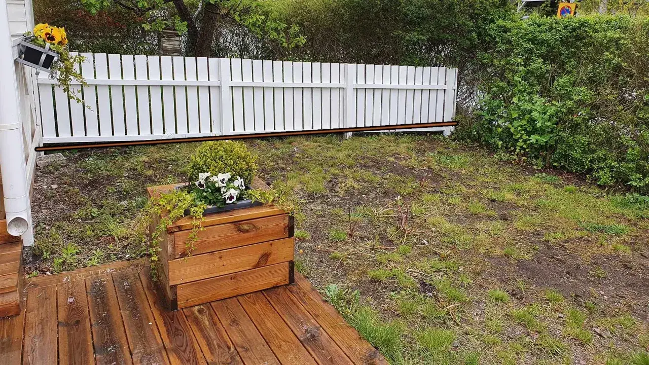 Tr&auml;d&auml;ck med en altan niv&aring;skillnad mot en sluttande gr&auml;smatta. En vit plankstaket avgr&auml;nsar.
