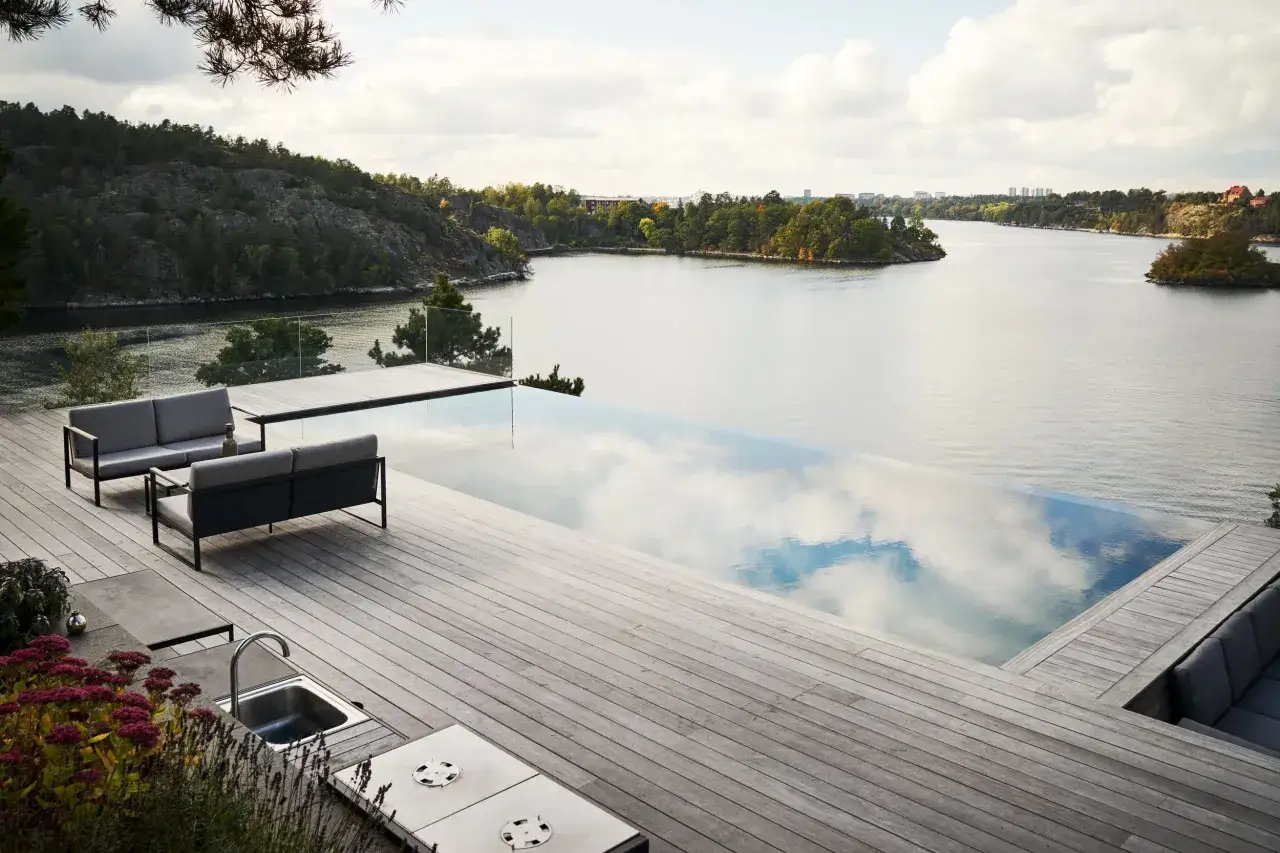 Drömmen om att bygga infinity pool vid vattnet blir verklighet. En modern terrass med loungegrupp och utekök.