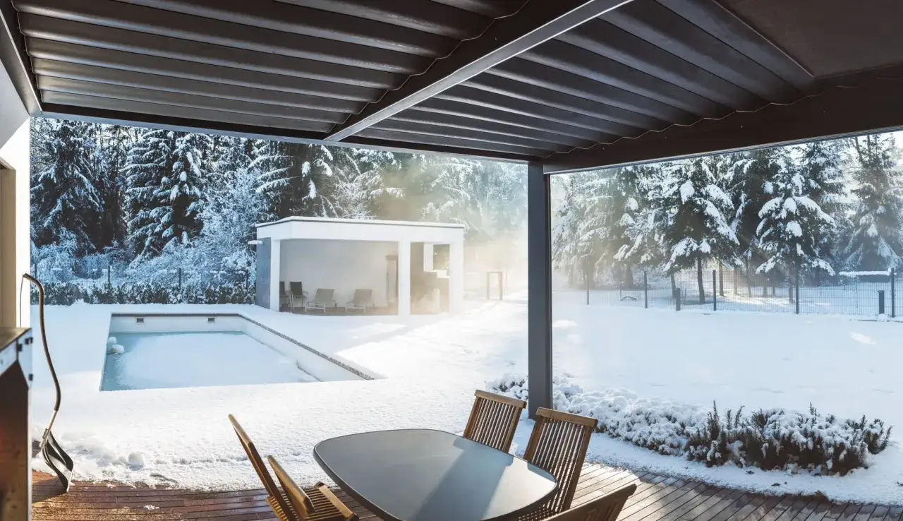 Vinterdag vid poolen. Sn&ouml; t&auml;cker allt utom poolen, som har isolering under poolen. Solen skiner genom tr&auml;den.