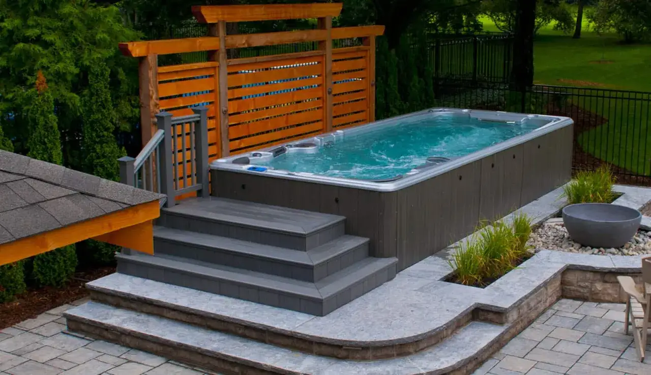 En lyxig swimspa med bubblande vatten, omgiven av en vacker tr&auml;dg&aring;rd. Perfekt swimspa inspiration f&ouml;r avkoppling och tr&auml;ning.