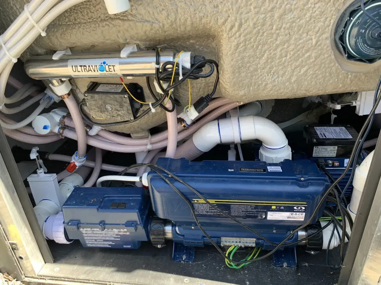 Insidan av ett spabad med UV-sterilisator, pumpar och rör. En bra affär för begagnade spabad.