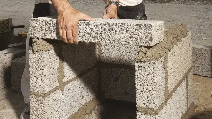 Händer lägger lecablock direkt på marken, bygger en mur med cement.
